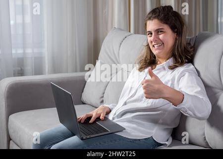 Disabled woman works on computer sitting on sofa at home Stock Photo