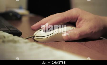 Close-up of man clicking on old computer mouse. Callused hand of office employee working at computer. Man uses old computer equipment Stock Photo
