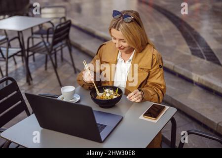 Beautiful woman eating asian food sitting at table outdoors Stock Photo