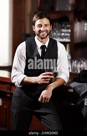 Relaxing while having a drink. Portrait of a well-dressed young man standing at a bar with a drink. Stock Photo