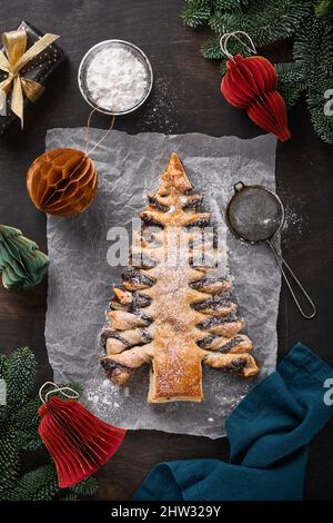 Puff pastry Christmas tree with chocolate paste, sprinkled with powdered sugar on old dark wooden background. Christmas or Xmas pastries. Top view. Co Stock Photo