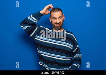 Horizontal shot of pensive handsome young European man scratching his head looking doubtfully to the side and having indecisive facial expression Stock Photo