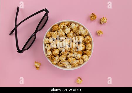 caramel popcorn in bowl and 3D glasses on pink background, home cinema, top view Stock Photo
