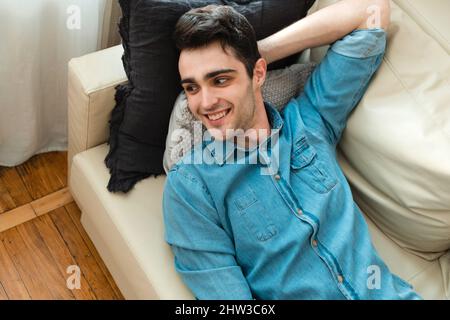 Young handsome man is relaxing on the sofa at home and thinking about the future. Caucasian millennial lies on the sofa, relaxes and looks away Stock Photo