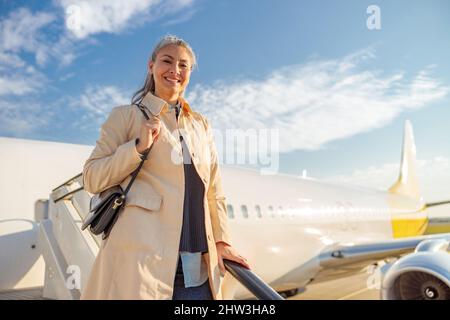 Cheerful woman standing on airplane stairs at airport Stock Photo