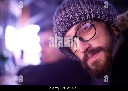 Portrait of a guy with glasses. Young man in a warm hat. The man at the bar. Portrait of a man with a European appearance. A man with poor eyesight. A Stock Photo