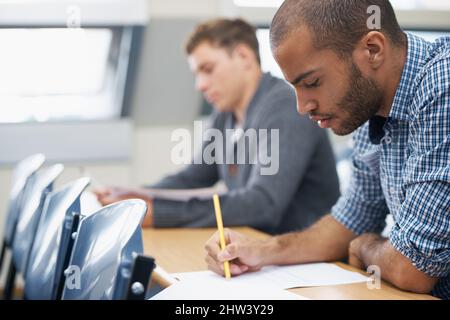 It all comes down to the test.... Two male students writing exam in a lecture hall. Stock Photo