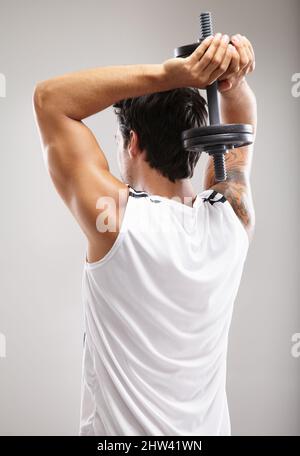 Working those biceps. Rearview of a young man using dumbbells to strengthen his triceps. Stock Photo