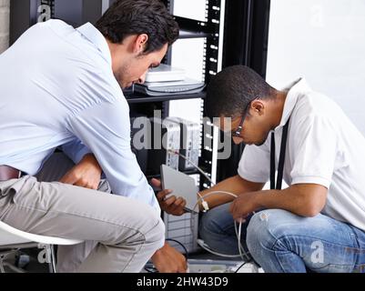 Finding the problem and correcting it. Two IT professionals working on a server. Stock Photo