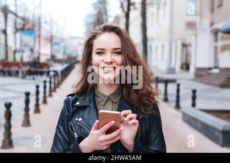 Focused woman walking and texting message on smartphone in city in spring day Stock Photo