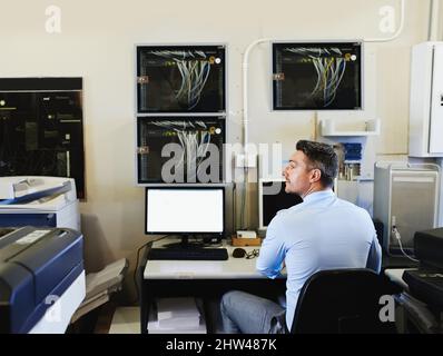 The technological heart of the company. Rearview shot of a computer engineer at work in a server room. Stock Photo