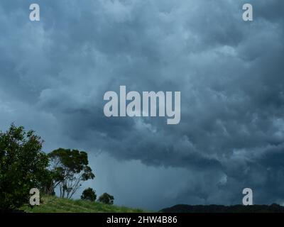Stormy weather, dark and grey sky with storms clouds, Trees and green grassy hillside, Summer storm threatening in coastal NSW Australia Stock Photo