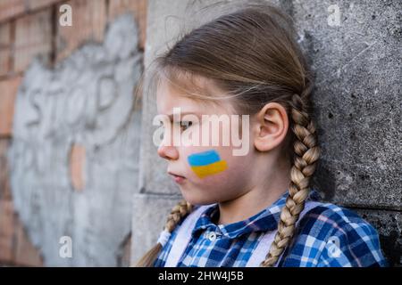 Portrait of a frightened child girl with painted flag on the cheek in yellow-blue colors of the Ukrainian flag. Peace and protection children concept Stock Photo