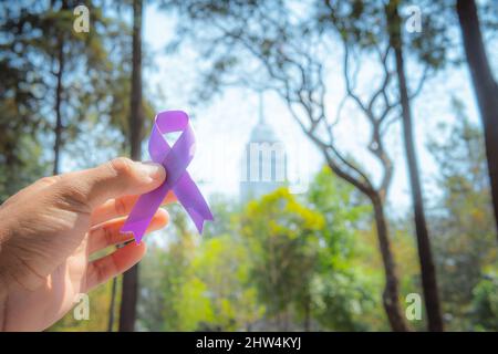 Adult hands with purple ribbon, Alzheimer's disease, Pancreatic cancer, Epilepsy awareness, World Cancer Day Stock Photo