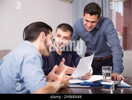 Three smiling men discussing papers at desk Stock Photo