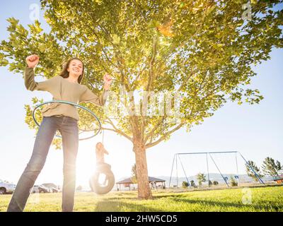 Girl (12-13) spinning hula hoop, sister (10-11) on tire swing in background Stock Photo