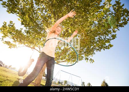 Girl (12-13) spinning hula hoop, sister (10-11) on tire swing in background Stock Photo