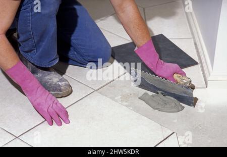 TILER KNEELING DOWN LAYING CERAMIC TILES IN THE BATHROOM OF A NEW HOME BEING BUILT IN SYDNEY, NEW SOUTH WALES, AUSTRALIA. Stock Photo