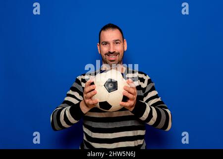Photo of young excited man happy positive smile hold ball game football fan champion isolated over blue color background Stock Photo
