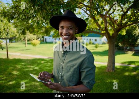 Mixed race male farmer standing outdoors typing on digital tablet Stock Photo