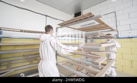 Workers transport wood frame at warehouse. Action. Two workers deliver wooden products and frames on rack with wheels to warehouse. Stock Photo