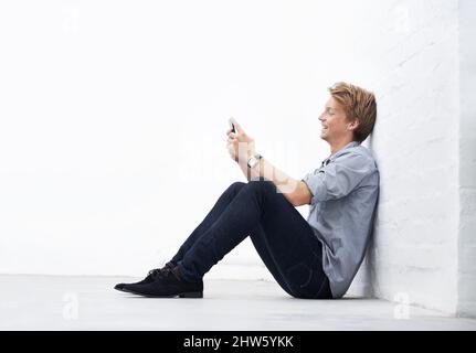 Sending an sms. A young man sitting in the studio and using his cellphone. Stock Photo