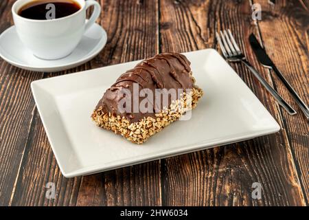 Dessert Cake from Malaga on wooden table. Cake with banana inside, covered with chocolate sauce and hazelnuts. Stock Photo