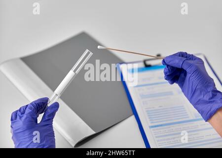 hands in gloves holding test tube and cotton swab Stock Photo