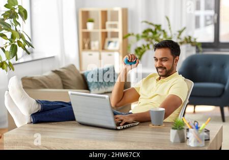 man with laptop and hand expander at home office Stock Photo
