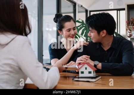 Real estate agent offer hand for customer sign agreement contract signature for buy or sell house. Happy asian couple signing a contract together at Stock Photo