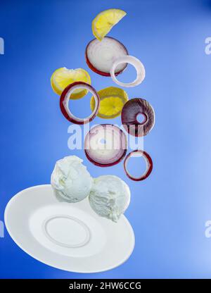 Levitating scoops of ice cream, red onion rings, lemon slices on a blue background Stock Photo