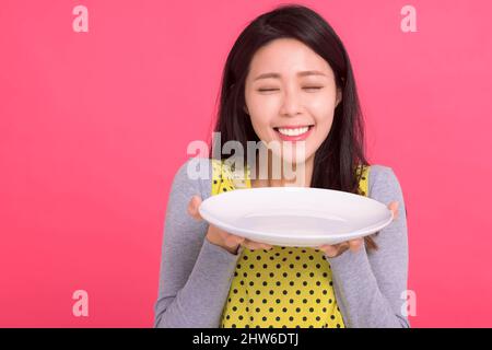 Happy young woman holding empty white plate and smelling Stock Photo