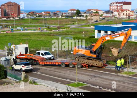 A Doosan orange digger being offloaded from a low loader trailer for use on a new construction site Cueto Santander Cantabria Spain Stock Photo