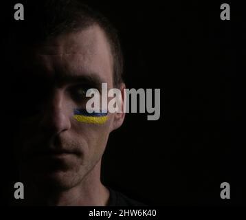 Portrait of patriotic Ukrainian man with painted yellow blue flag on his face. Dark background, space for text Stock Photo