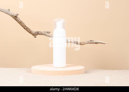 White blank plastic packaging cosmetic pump bottle for mousse foam cream stand on round podium platform with beach sand and beige background. Front Stock Photo