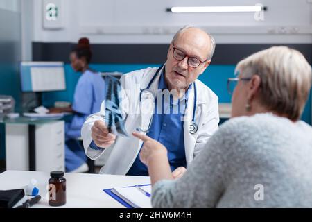 Specialist and patient analyzing radiography results to find diagnosis and treatment, looking at x ray scan exam. General practitioner explaining bones disease and talking about medicine Stock Photo