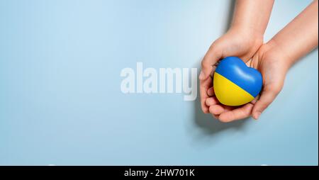 High angle view of human hands holding heart, painted with ukraine flag colors isolated on blue background