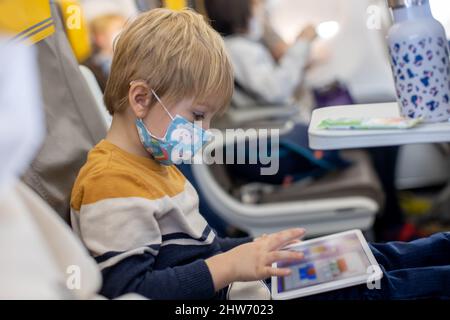Mother and child, boy and mom, sitting in airplane, child playing on tablet, family trip Stock Photo