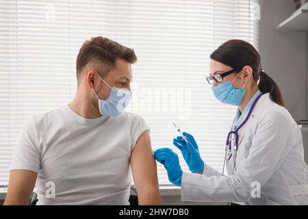 The doctor holds a syringe before giving an injection to a patient in a medical mask. Covid-19 or coronavirus vaccine. Vaccination of the population Stock Photo