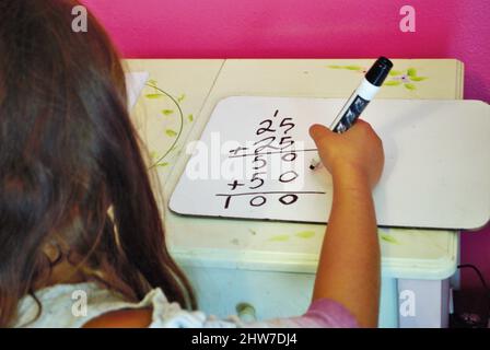 Second grade girl learning how to carry the one on a whiteboard while distance learning not common core math Stock Photo