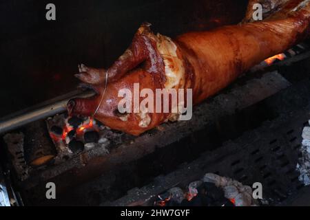 Pig is being grilled slowly on spit in traditional way, cooked with charcoal, fatty roasted meat Stock Photo