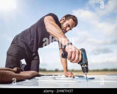 Man working with a cordless drill on the roof of a van Stock Photo