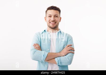 Portrait of a cheerful young man in a white T-shirt on a white background. The guy is standing looking at the camera and smiling. Stock Photo