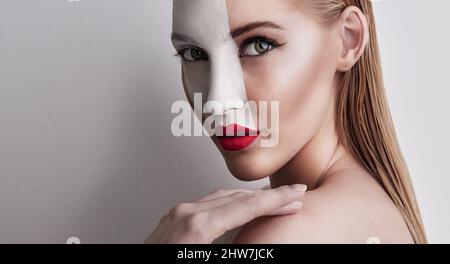 Living in a world of red and white. Shot of a beautiful woman wearing face paint and red lipstick against a plain background. Stock Photo