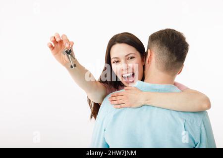 A cheerful young couple is hugging in the kitchen, holding the keys to a new house in their hands. Happy newlyweds moved into a new apartment, got a Stock Photo