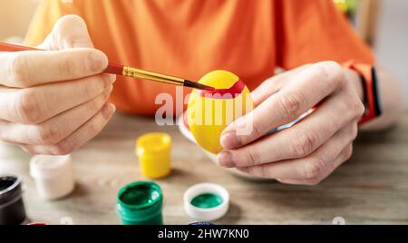 Woman's hand with a brush is drawing a colored pattern on an Easter egg. Creative preparation for bright Easter holiday Stock Photo