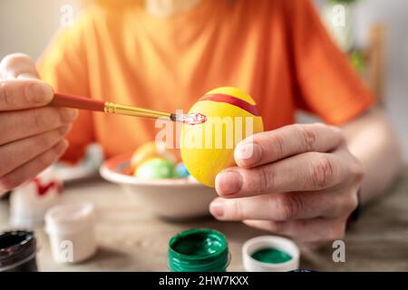 Woman's hand with a brush is drawing a colored pattern on an Easter egg. Creative preparation for bright Easter holiday Stock Photo