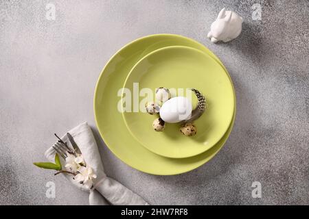 Easter table setting with green plate, spring blossom flowers and organic eggs on gray background. View from above. Space for text. Stock Photo