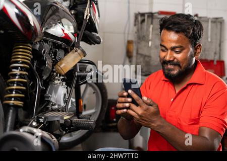 Young smiling mechanic using mobile phone in front of motors in showroom - concept of relaxation, taking break time and reading messages Stock Photo