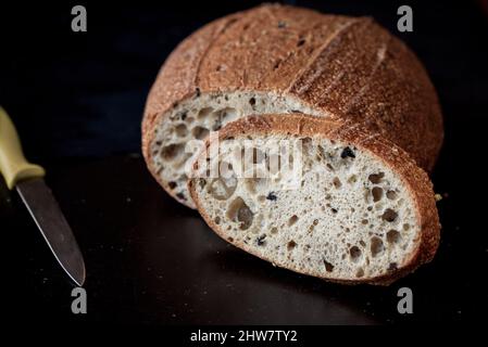 Homemade thyme bread with a knife on a black wooden slate, close up, isolated Stock Photo